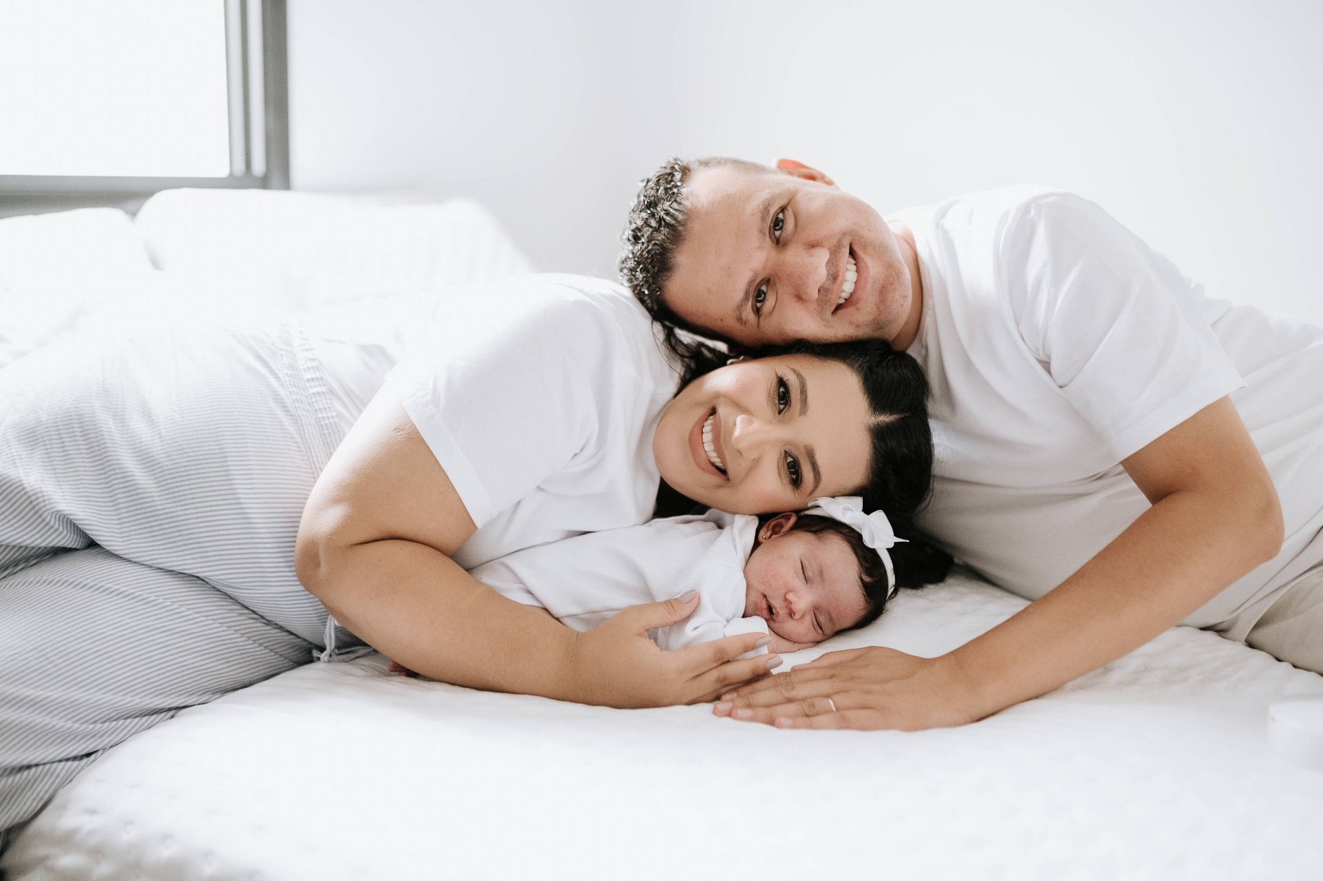 Pai, mãe e recém-nascido deitados juntinhos na cama