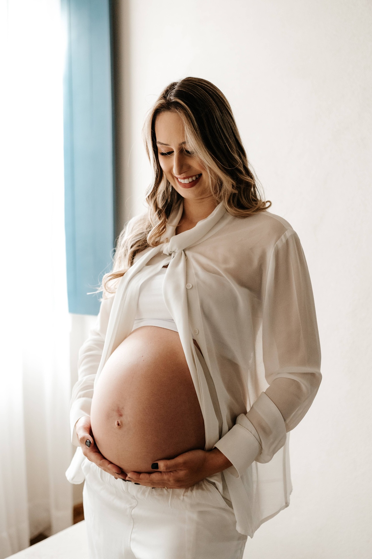 Gestante de camisa branca olhando para a barriga